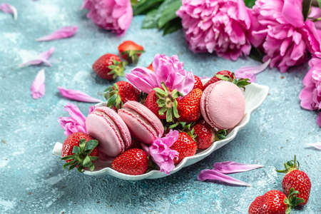 Pink peony rose flower and macaroni cookies and sweet strawberry on blue background. Small French cakes Macarons with fruit. top view.の写真素材