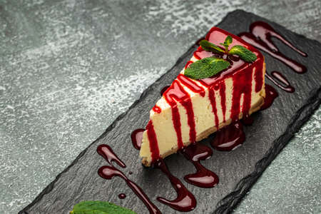 Piece of cheesecake with fresh strawberries jam and mint. Tasty homemade cheesecake on a dark background.の写真素材
