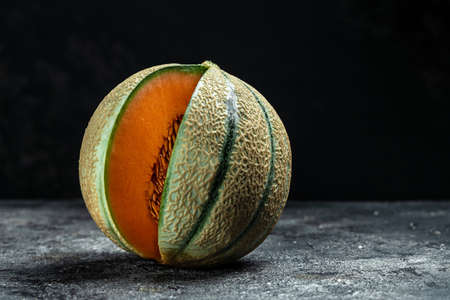 Raw Organic Tuscan Melon Cantaloupe. Yellow pieces of melon on a wooden board on a dark background,...