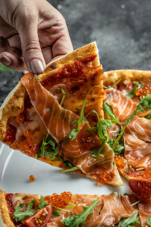 Delicious hot pizza with salmon, red caviar, tomatoes and aragula ready to eat. vertical image. top view. place for text.の写真素材