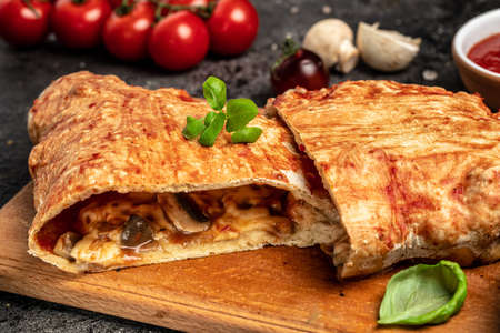 Calzone pizza with tomatoes, mozzarella, mushrooms and fresh basil, italian calzone vegetarian pizza, Food recipe background. close up,の写真素材