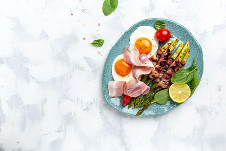 The ketogenic diet. Keto brunch breakfast. fried eggs, asparagus wrapped in bacon, ham, tomatoes and...