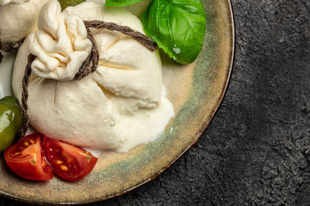 Italian tomatoes and burrata cheese salad served with cherry tomatoes, fresh basil leaves, prosciutto ham and olives on a dark background. Restaurant menu top view.の写真素材