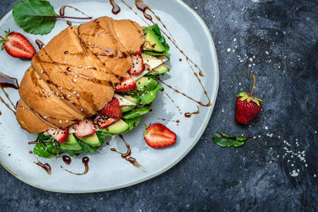Sandwich Croissant with avocado, strawberries, brie camembert cheese, fresh salad in a whole wheat bread with seeds. Healthy diet concept. banner, menu, recipe, top view.の写真素材