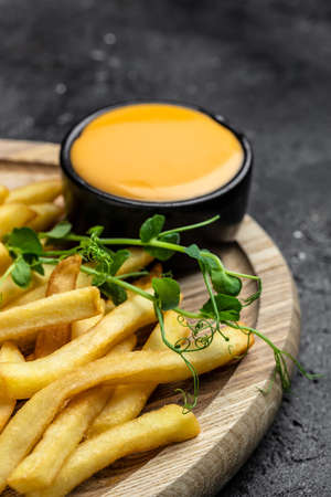 Fresh hot french fries with cheese sauce on a dark concrete background, Restaurant menu, dieting,...