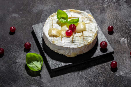 french cuisine. Baked camembert cheese with cranberries and basil leaves on a dark background,...