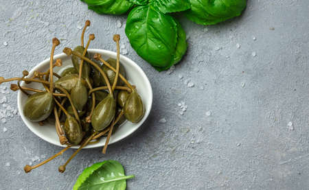 Capers. Marinated or pickled canned capers fruit with fresh basil leaves in a small bowl, on a gray background. Long banner format. top view.の写真素材