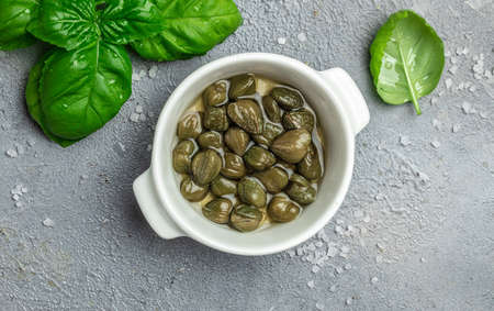 Marinated capers with fresh basil leaves in a small bowl, on gray background. Long banner format. top view.の写真素材