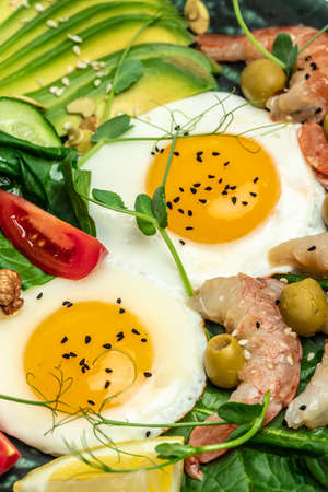 Ketogenic diet breakfast shrimps, prawns, soft fried egg, fresh salad, tomatoes, cucumbers and avocado on a dark background. Keto, paleo lunch. vertical image. top view.の写真素材