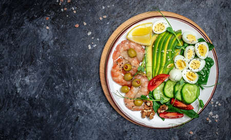 Ketogenic breakfast. Keto low carb shrimps, prawns, quail eggs, fresh salad, tomatoes, cucumbers and avocado on a dark background. keto diet. top view.の写真素材