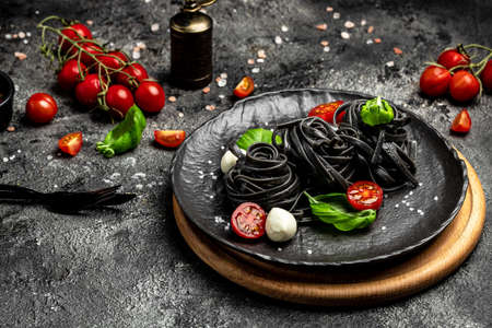 black pasta caprese salad tomatoes, mozzarella and green basil leaves. Pasta with cuttlefish ink. Vegan or gluten free diet. top view. place for text.の写真素材