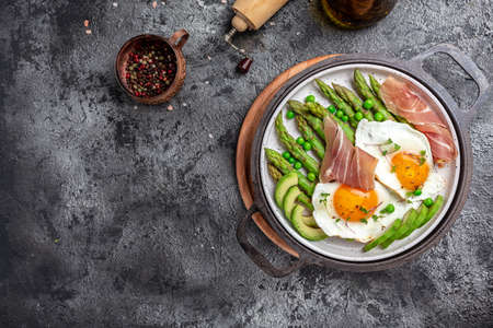 Tasty breakfast. avocado, asparagus, jamon, ham, prosciutto and fried egg on white plate. The ketogenic diet. Low carb high fat breakfast, top view.の写真素材