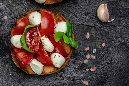 Caprese toasts with mozzarella, cherry tomatoes and fresh garden basil. Traditional italian appetizer or snack, antipasto. top view. place for text,の写真素材