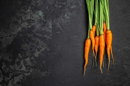 Fresh and sweet carrot bunch on dark background. Healthy vegan food. banner, menu, recipe place for text, top view.の写真素材