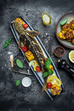 Grilled Sturgeon fish with vegetables, lemon, herbs and spices on a dark background, vertical image. top view. place for text,の写真素材