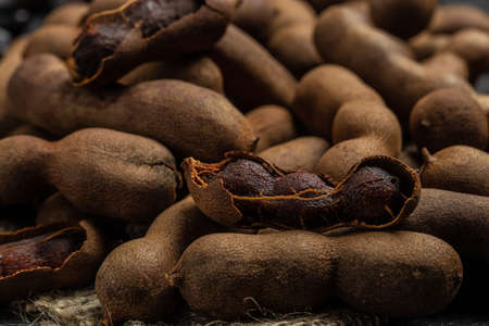 Tropical fruits, Tamarindo beans in shell on a brown butchers block on a dark background, healthy fruit. banner, menu, recipe place for text, top view.の写真素材