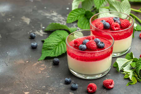 Delicious italian dessert panna cotta with berry sauce on a dark background in small jars. place for text.の写真素材