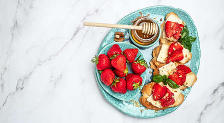 Two toasts or bruschetta with trawberries, cheese camembert nuts and honey. Summer breakfast. Healthy, clean eating. Vegan or gluten free diet.の写真素材