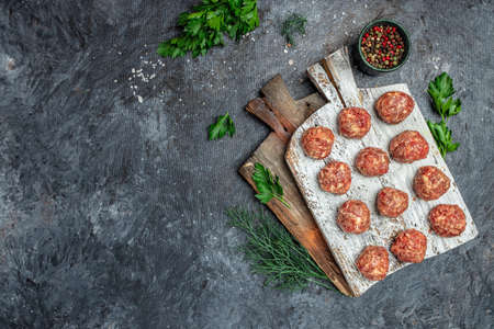 Fresh raw beef meatballs with spices on a cutting board on a dark background, banner, menu, recipe place for text, top view.の写真素材