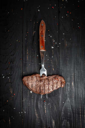 Grilled beef steak on a fork adding rosemary on black background. banner, menu, recipe place for text, top view.の写真素材