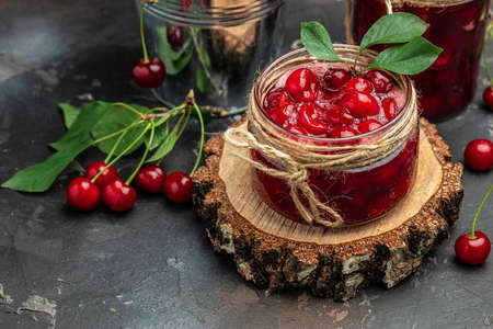 Cherry confitur jam in a jar and fresh berries on the table. Preserved organic food from garden on a dark background. banner, menu, recipe place for text.の写真素材