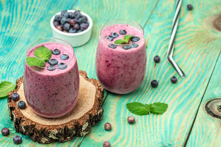 yogurt smoothies fresh blueberries in glass with mint leaf and raw berries on blue background. Restaurant menu, dieting, cookbook recipe top view.の写真素材