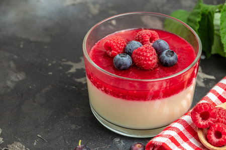 Delicious italian dessert panna cotta with berry sauce on a dark background in small jars. place for text.の写真素材