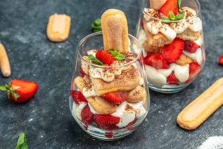 Tiramisu. Homemade tiramisu with fresh strawberry, mascarpone and mint in glass on dark background. Vegan lactose free dessert, Recipe of healthy organic decert.の写真素材