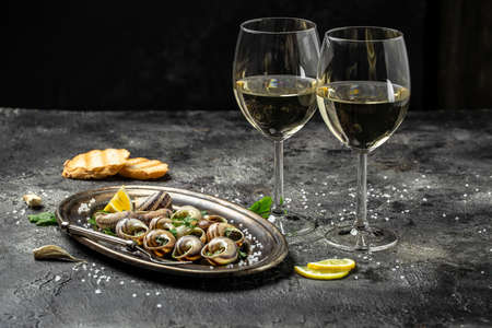 Delicious cooked sea escargo snails with herbs, butter, garlic on metal plate with forks. wine glass. gourmet food. Restaurant menu, Traditional French cuisine,の写真素材