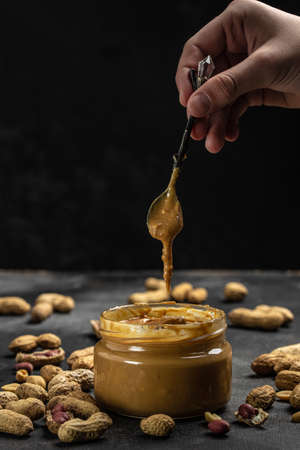 peanut paste in an open jar in spoon near creamy peanut butter peanuts scattered on a dark background, place for text, top view.の写真素材