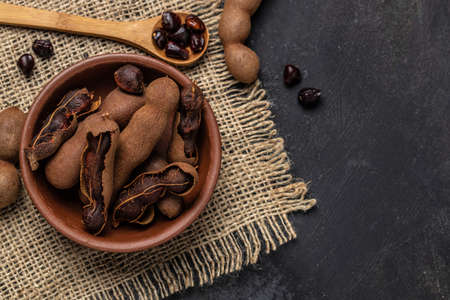 Tropical fruits, Tamarindo beans in shell on a brown butchers block on a dark background, healthy fruit. banner, menu, recipe place for text, top view.の写真素材