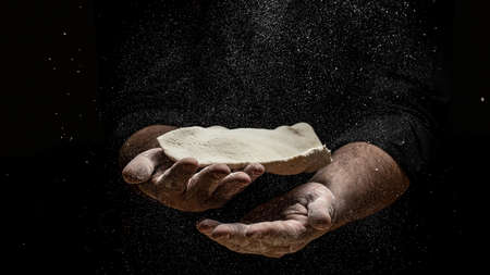 Beautiful and strong men's hands knead the dough make bread, pasta or pizza. Powdery flour flying into the air. chef hands with flour in a freeze motion of a cloud of flour midair.の写真素材