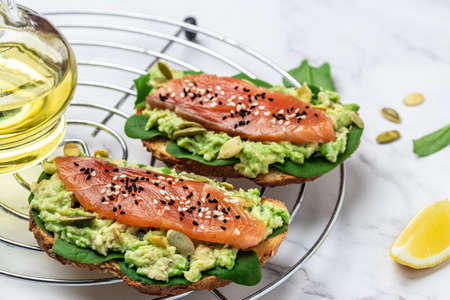 Delicious breakfast or snack sandwich salmon, avocado, spinach, nuts, sunflower seeds, toast with red fish and guacamole. Healthy, clean eating. Vegan or gluten free diet. top view, copy space.の写真素材