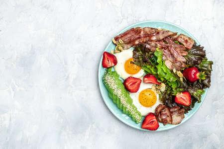 Ketogenic diet food, Fried egg bacon with avocado, strawberries and fresh salad on a light background. healthy meal concept, Long banner format. top view.の写真素材