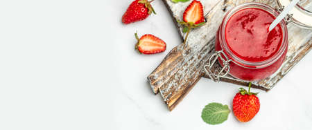 Jar of strawberry jam and fresh berries on wooden board white background. Long banner format.の写真素材