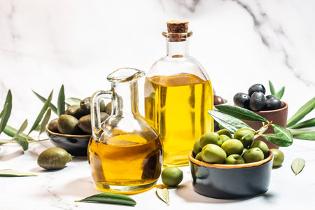 Olive oil in two glass containers and harvest olives berries in bowls on a light backgroundの写真素材