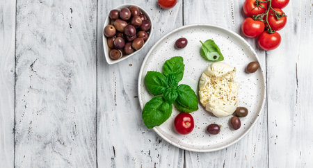 Creamy Italian Burrata Cheese with basil, olive oil and cherry tomatoes on white plate on light wooden background. Long banner format. top view.の写真素材