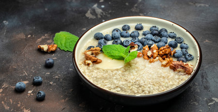 Oatmeal porridge in a bowl with fresh blueberries and nuts on a dark table. Healthy breakfast. Super food healthy eating vegetarian vegan food. Long banner format. top view.の写真素材