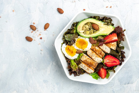 Ketogenic low carb diet. Plate with keto foods: two eggs, avocado, grilled chicken fillet, nuts, strawberries and fresh salad. Healthy fats, clean eating for weight loss. view.の写真素材