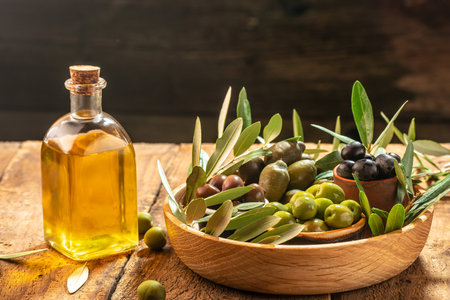 olives berries in wood bowls and pressed oil in glass bottles on a wooden background. place for text.の写真素材
