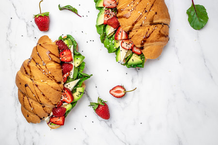 Sandwich Croissant with avocado, strawberries, brie camembert cheese, fresh salad in a whole wheat bread with seeds. Healthy diet concept. banner, menu, recipe, top view.の写真素材