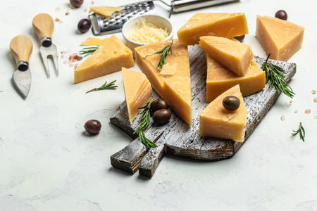 Parmesan cheese on a wooden board, Hard cheese, olives, rosemary and metal grater on a light background. place for text, top view.の写真素材