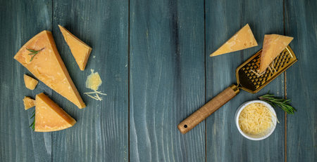 Parmesan cheese on a wooden board, Hard cheese, olives, rosemary and metal grater on a light...
