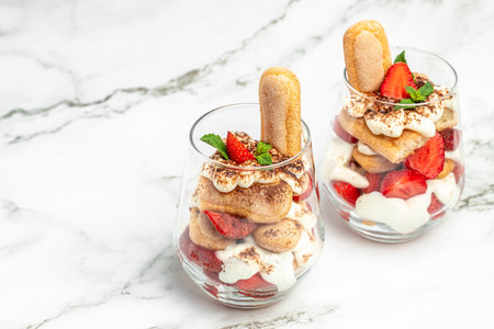 Tiramisu. Homemade tiramisu cake with fresh strawberry, mascarpone and mint in glass. Tiramisu portion on plate on dark background. Delicious no bake tiramisu.の写真素材