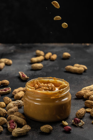Peanut butter in glass jar and spoon on dark background, American dessert concept. vertical image. top view. place for text.の写真素材