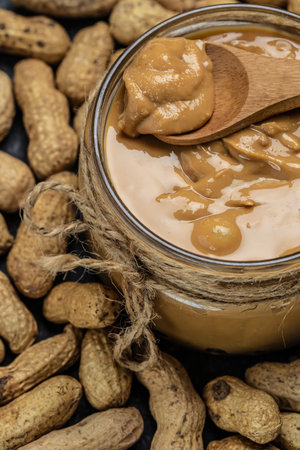 Peanut butter in glass jar and spoon on dark background, American dessert concept. vertical image. top view. place for text.の写真素材