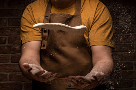 flying pizza dough with flour scattering in a freeze motion of a cloud of flour midair on black. Cook hands kneading dough. copyspace.の写真素材
