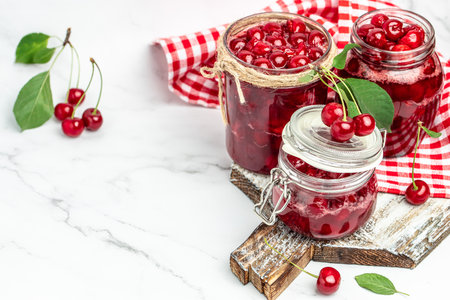 Jar of cherry jam and sour cherries. Berries cherry with syrup. Ripe ripe cherry. Sweet red cherry. Canned fruit on a wooden background.の写真素材