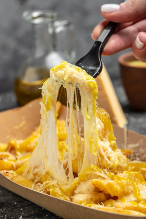 Cheddar Cheese Poured or Pulled from on top Deep Fried French Fries on a dark background, Fast food...