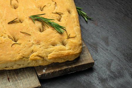 Focaccia bread with rosemary and olive oil on a wooden board. on a dark background. banner, menu, recipe place for text, top view.の写真素材